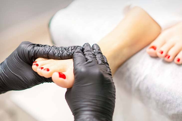 Foot massage with moisturizing and peeling cream by pedicurist hands wearing black gloves close up