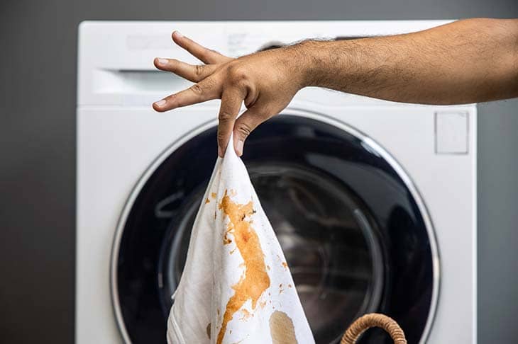 Man holds shirt stains dirty washing machine