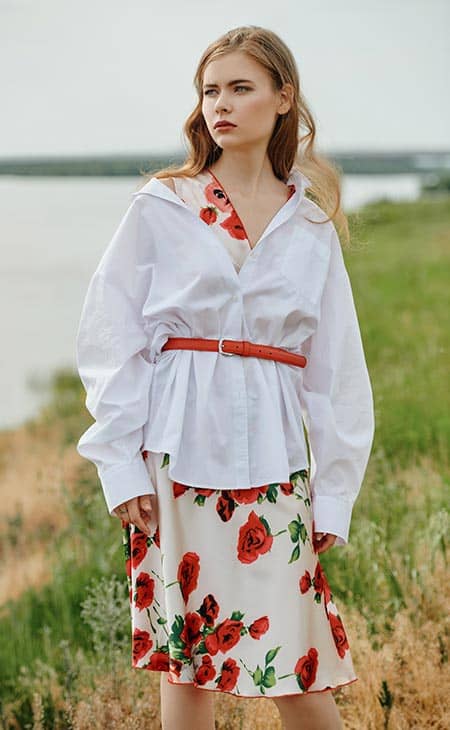 Chica camisa blanca clara y un vestido floral se encuentra pensativamente en la orilla del rio