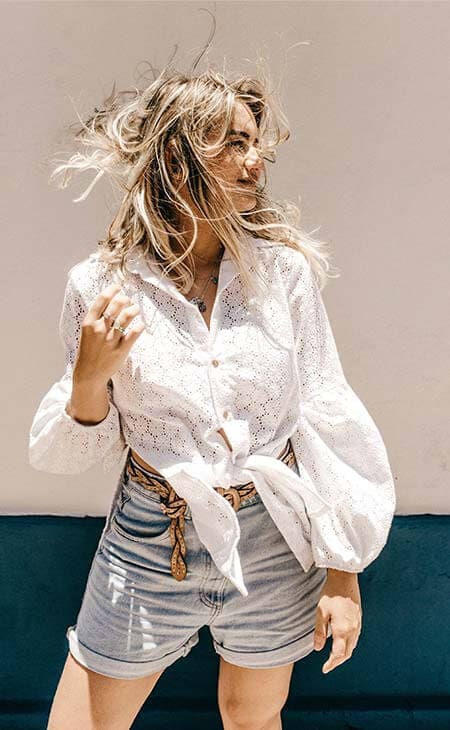 Young blonde woman wearing brown short pants with belt and white tshirt  arranging messy hair, summer fashion clothing, casual female shorts outfit  Stock Photo