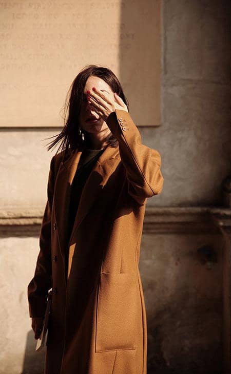 Woman brown coat covers face hand