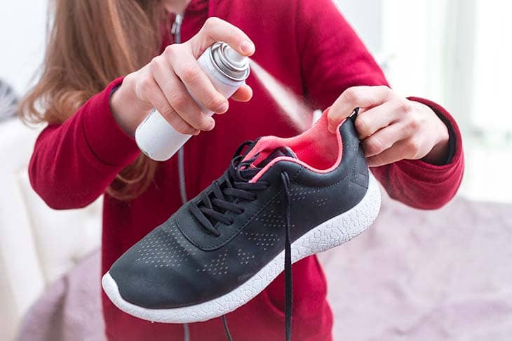 A young woman spraying deodorant on sweaty running shoes for eliminate unpleasan sport footwear needs in cleaning and odor removal